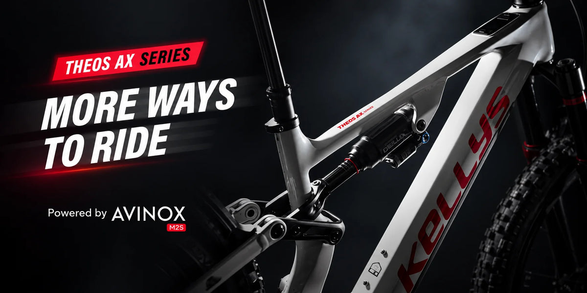 Close-up promotional shot of a white mountain bike frame with red 'Kellys' branding, shown against a dark dramatic background with text reading 'THEOS AX SERIES', 'MORE WAYS TO RIDE', and 'Powered by AVINOX'.